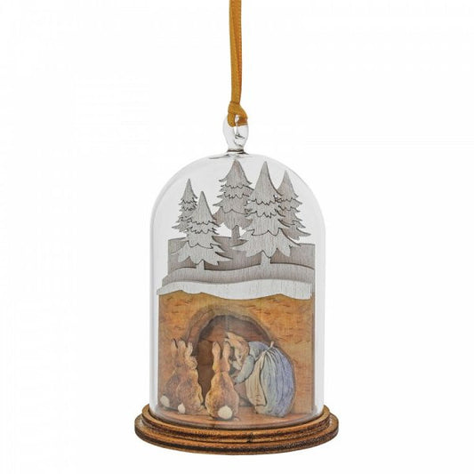 The Beatrix Potter Mrs. Rabbit in Burrow Wooden Hanging Ornament features Mrs. Rabbit in blue kneeling by a burrow with three brown rabbits, winter trees, a snowy scene under a glass dome, and comes with a wooden base and hanging ribbon.