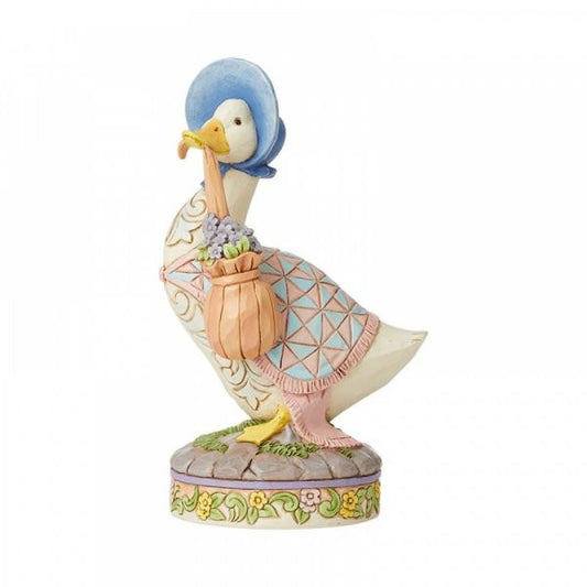 The ..wearing a shawl and a poke bonnet Jemima Puddle-Duck Figurine by Jim Shore, from Beatrix Potter by Jim Shore, features Jemima with her signature blue bonnet, patterned shawl, and a pink basket of purple flowers on a floral base.