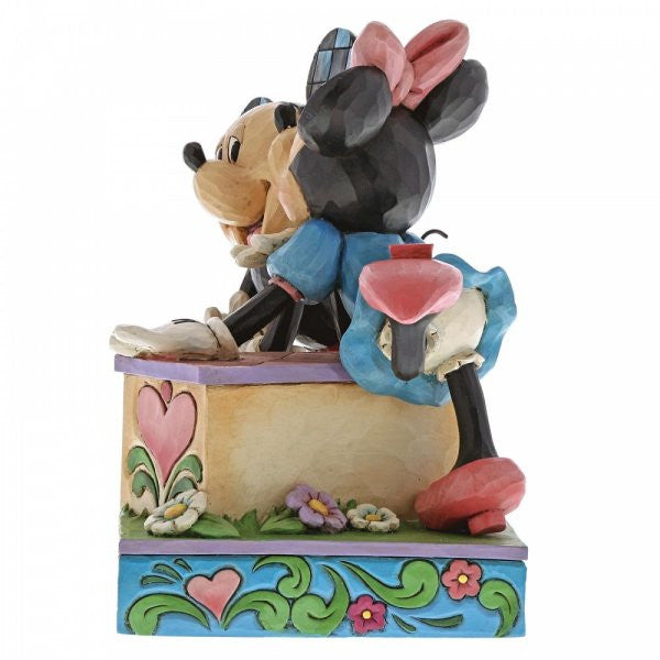 Disney Traditions Minnie leans over a kissing booth to plant a smooch on one very smitten Mickey Mouse figurine