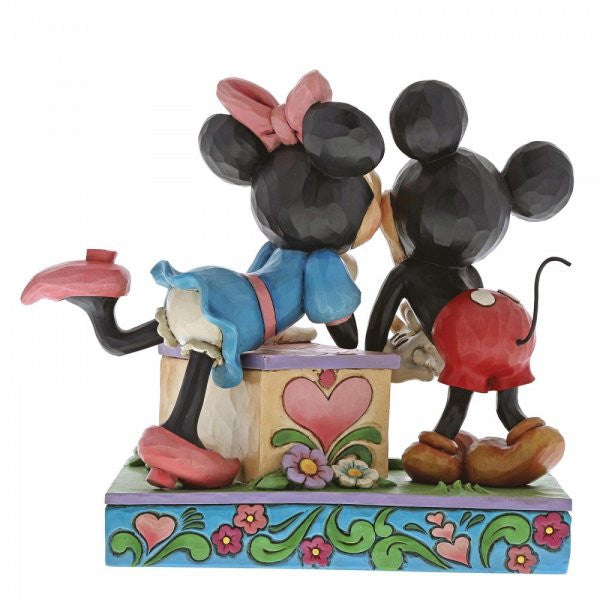 Disney Traditions Minnie leans over a kissing booth to plant a smooch on one very smitten Mickey Mouse figurine