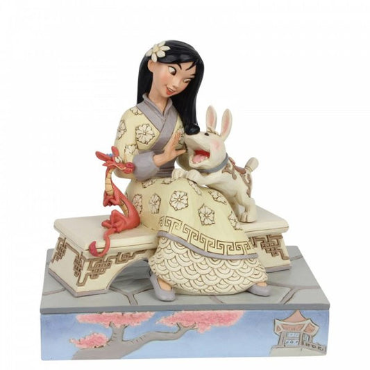 Disney Traditions Mulansitting on a bench in her best dress with her excitable pup, Little Brother, bouncing in her lap and her dragon guardian Mushu figurine