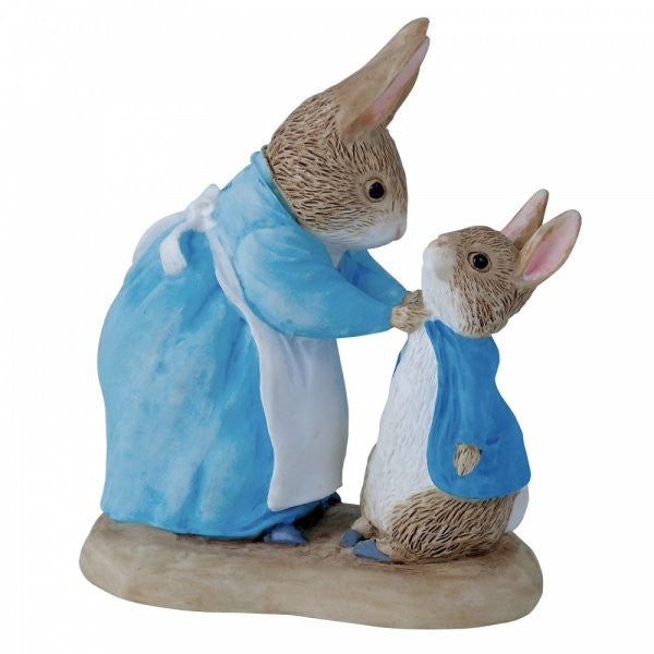 The Beatrix Potter Mrs. Rabbit & Peter figurine features Mrs. Rabbit in a blue dress and apron helping Peter, who wears a blue coat. Both stand on a base, inspired by the classic Beatrix Potter characters.