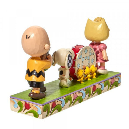 The Peanuts Parade Figurine by Jim Shore features Charlie Brown with a bat, Snoopy with a bass drum, Sally in pink, and two yellow birds on a decorative base with classic Jim Shore detailing. Brand: Peanuts By Jim Shore.
