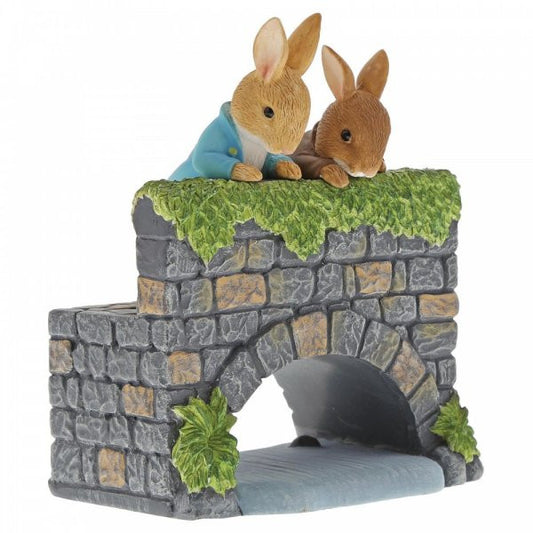The Beatrix Potter Peter & Benjamin Bunny on the Bridge Figurine features two rabbits leaning over a stone bridge with lush greenery, making it a charming collectable gift.