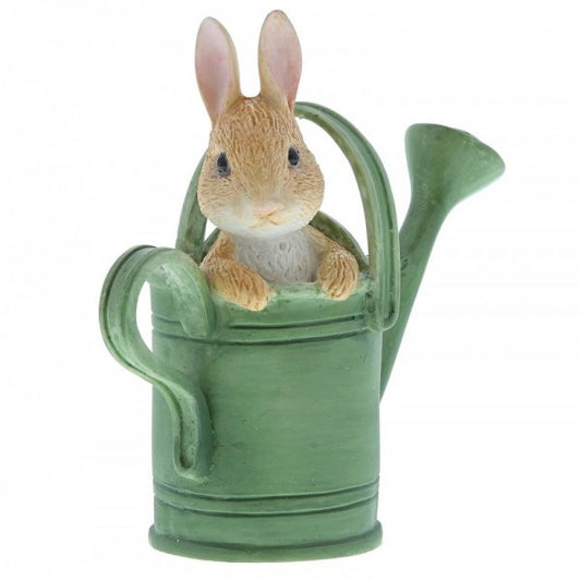 The Beatrix Potter Peter in Watering Can Mini Figurine features Peter with pink ears peeking from a green can, adding a charming touch. The background is white.