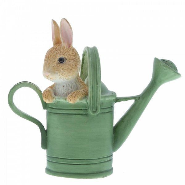 The Beatrix Potter Peter in Watering Can Mini Figurine features a small brown rabbit playfully peeking out from a green watering can, front paws on the edge, capturing whimsical charm.
