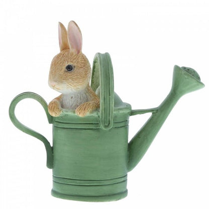The Beatrix Potter Peter in Watering Can Mini Figurine features a small brown rabbit playfully peeking out from a green watering can, front paws on the edge, capturing whimsical charm.