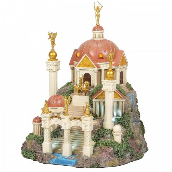 Themyscira Building DC Village by Department 56 is a miniature model featuring tall columns, domes, golden statues, and a waterfall atop a rocky green landscape—capturing the grand, Greek-inspired temple of Wonder Woman’s home.