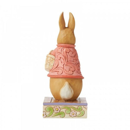 The ‘Good Little Bunny’ Flopsy Bunny Figurine by Jim Shore features a rabbit in a pink coat with a basket on a floral base—an ideal Beatrix Potter collectible from the Beatrix Potter by Jim Shore collection.