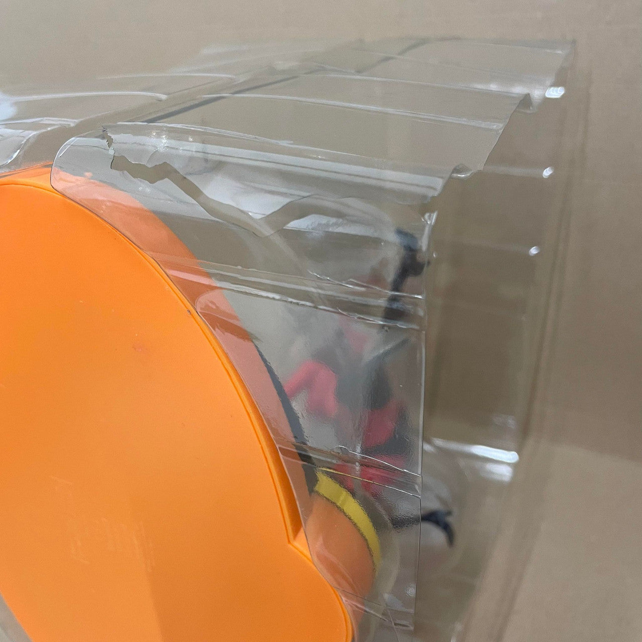 A cracked plastic packaging box labeled DAMAGED BOX - Grand Jester Studios Disney Mrs Incredible Vinyl Figurine holds an orange circular item and the partially visible Mrs Incredible figure. The plain background is beige.