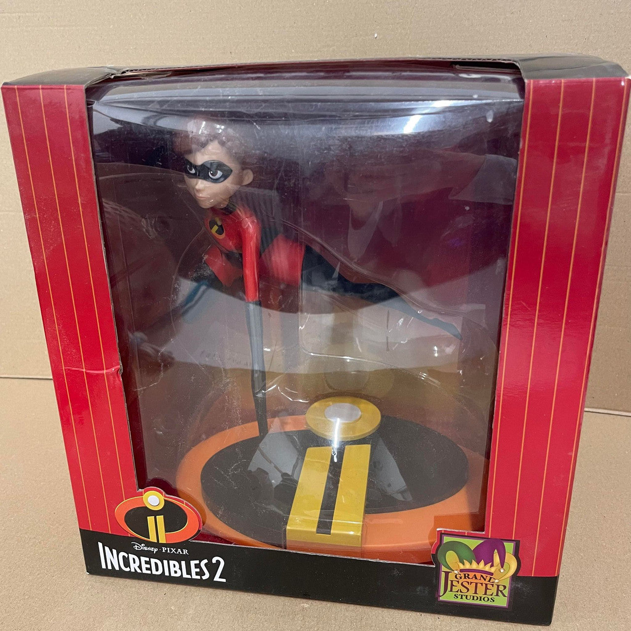 A DAMAGED BOX - Grand Jester Studios Disney Mrs Incredible Vinyl Figurine features Mrs Incredible in her superhero suit, posed on a display base inside clear packaging with red and yellow accents. Brand: Grand Jester Studios.