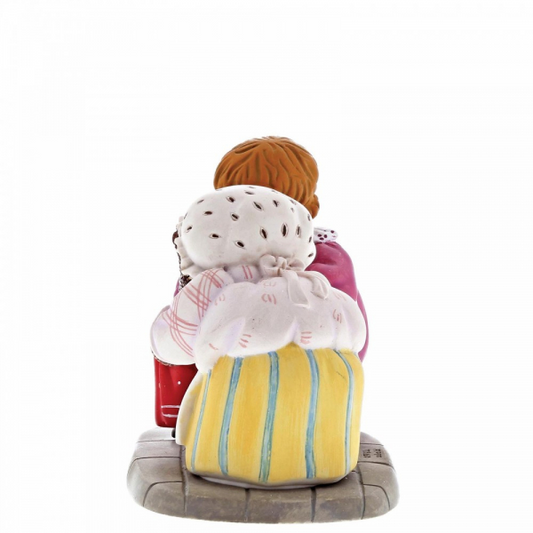 The Beatrix Potter Mrs. Tiggy Winkle and Lucie Figurine by Beatrix Potter depicts a collectable scene of Lucie with brown hair, viewed from behind, sitting on a bench with two large, colorful cloth bundles.