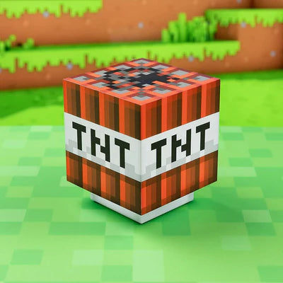The Minecraft TNT Light With Sound by Paladone, a blocky red and white TNT cube, sits on pixelated green grass, perfectly capturing the essence of Minecraft with blurred dirt and grass blocks in the background.