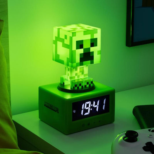 The Minecraft Creeper Icon Alarm Clock by Paladone glows green on a nightstand, showing 18:41. Nearby, a game controller and monitor complete the perfect Gamer’s Bedroom setup.