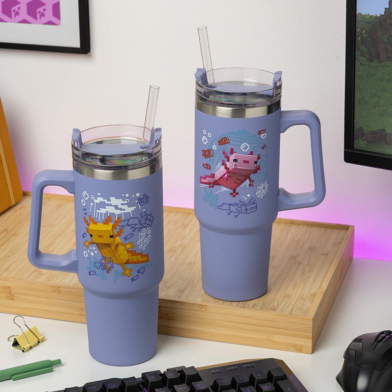 Two large purple Minecraft Insulated Cups with straws and handles by Paladone feature pixel art axolotl designs. Shown on a wooden tray near office supplies, theyre perfect for any Minecraft gamer’s collection.